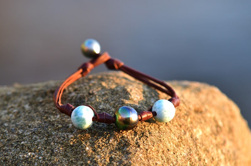 Leather bracelet with one Tahitian pearl and Larimar displayed on a rock facing the sea
