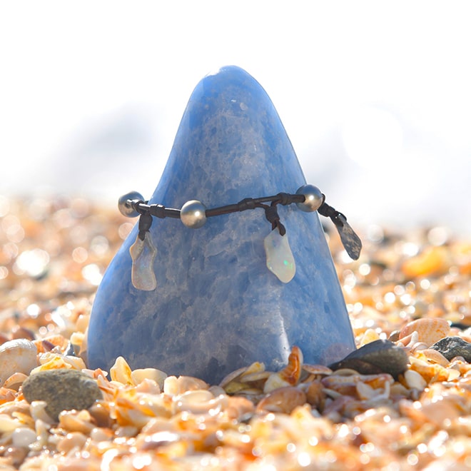 Leather bracelet or anklet with opals and Tahitian cultured pearls displayed around a blue stone on the beach