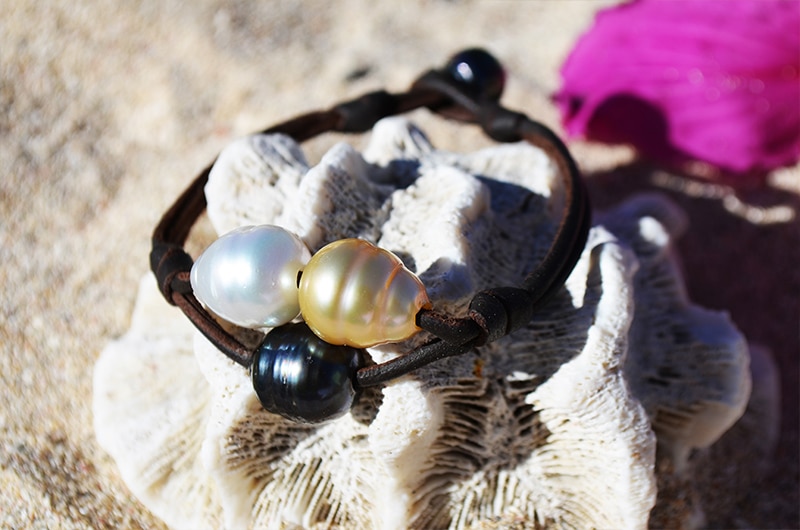 Two-row leather bracelet with three multicolored pearls displayed in a dark seashell