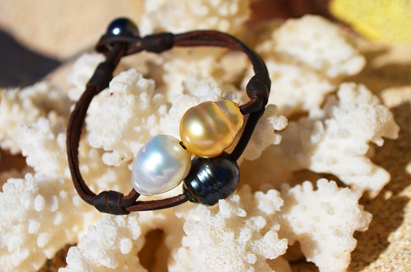 Close-up of the two-row bracelet with three multicolored pearls displayed on coral