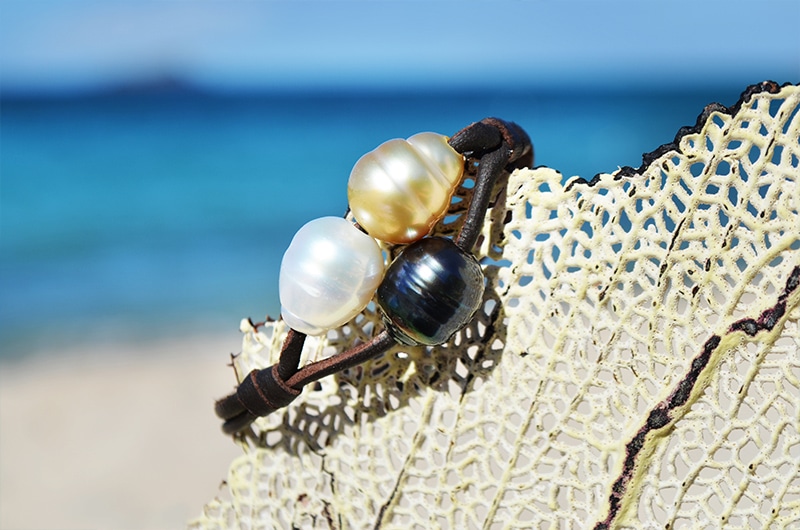 Two-row bracelet with three multicolored pearls displayed on a sea fan facing the ocean