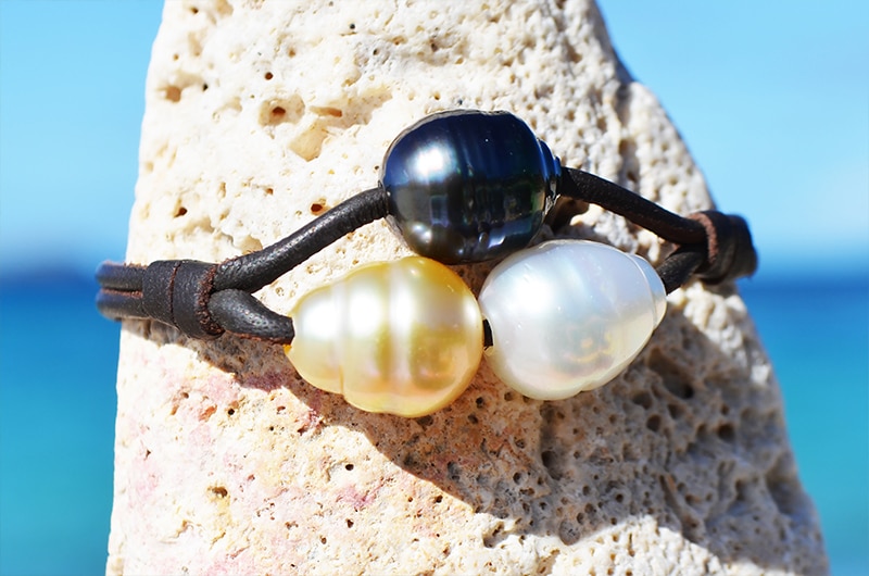 Two-row leather bracelet with three multicolored pearls displayed on a pale rock