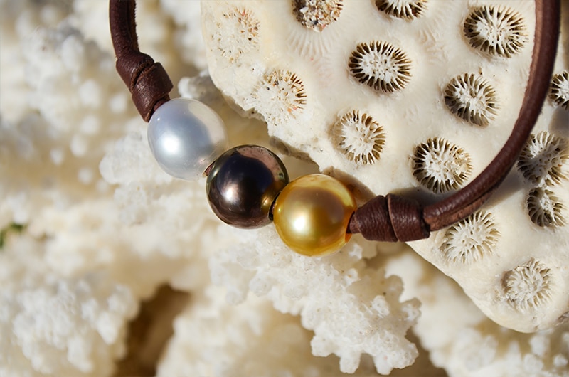 Close-up of the bracelet with three multicolored pearls displayed on coral