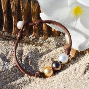 Bracelet avec trois perles multicolores présenté sur le sable près de fleurs blanches
