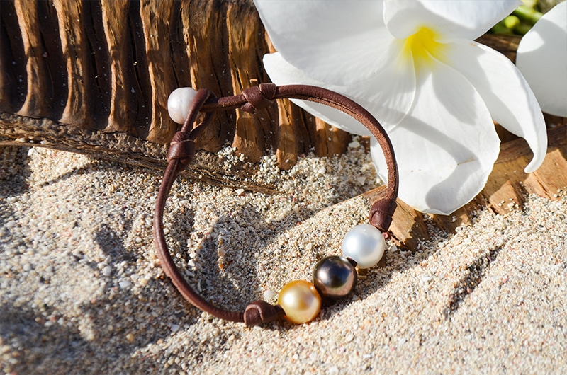 Bracelet with three multicolored pearls displayed on the sand near white flowers