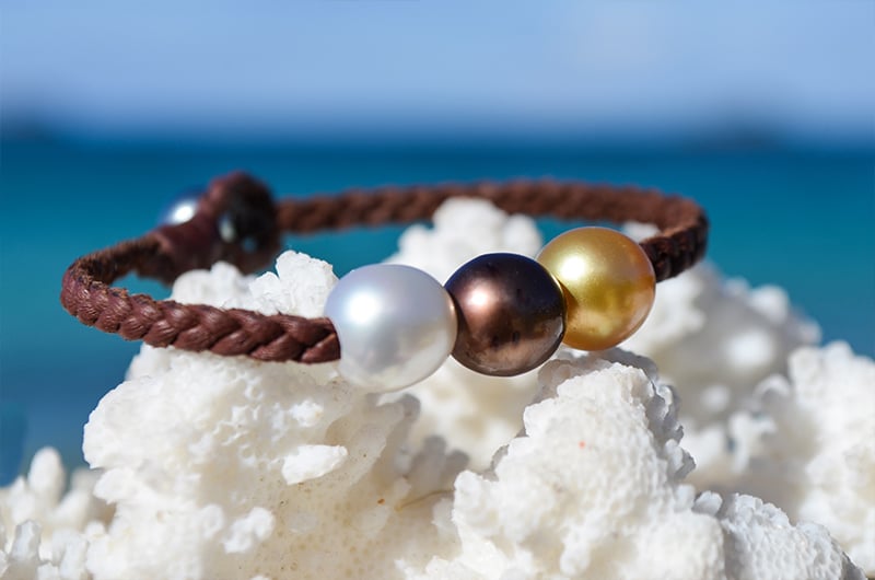 Bracelet tressé avec trois perles multicolores présenté sur du corail face à la mer