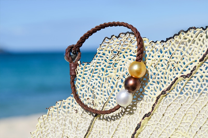 Vue d’ensemble du bracelet tressé avec trois perles multicolores présenté sur un éventail de mer