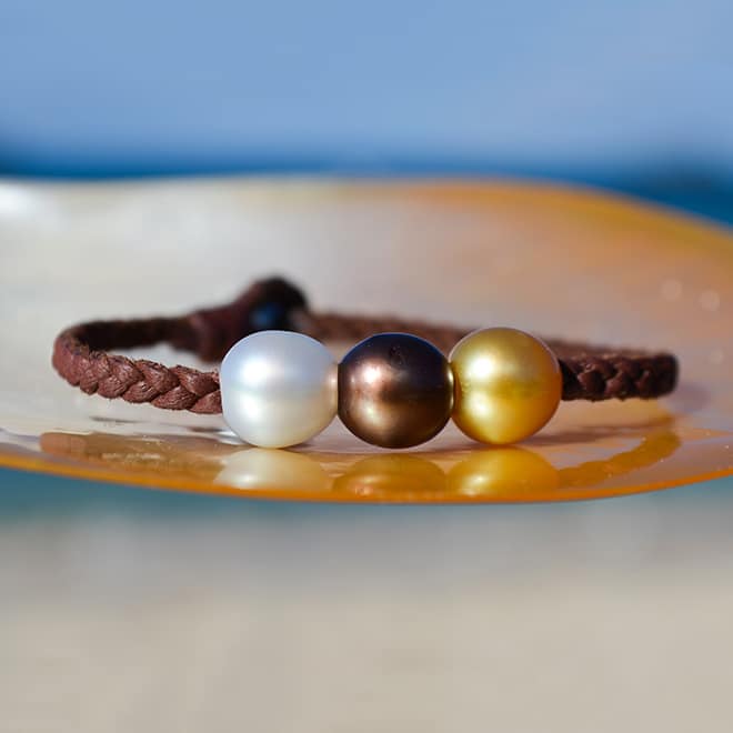 Bracelet en cuir marron tressé avec trois perles de culture multicolores de 9 mm présenté sur une nacre