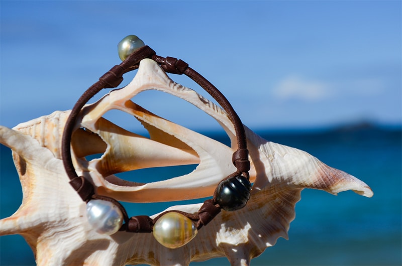 Leather bracelet with three multicolored circled pearls displayed in a seashell facing the sea