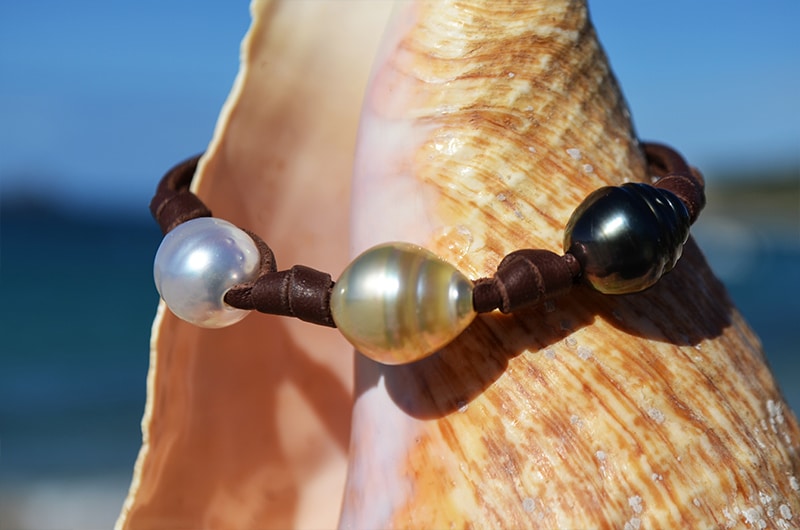Detail of the three multicolored circled pearls and knots on the leather bracelet displayed on a seashell