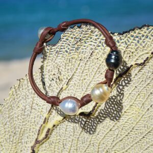 Bracelet en cuir marron avec trois perles de culture cerclées multicolores et nœuds présenté sur un éventail de mer
