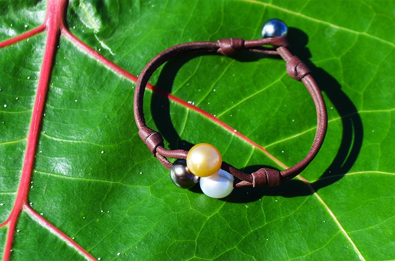 Two-row leather bracelet with three multicolored pearls displayed on a green leaf