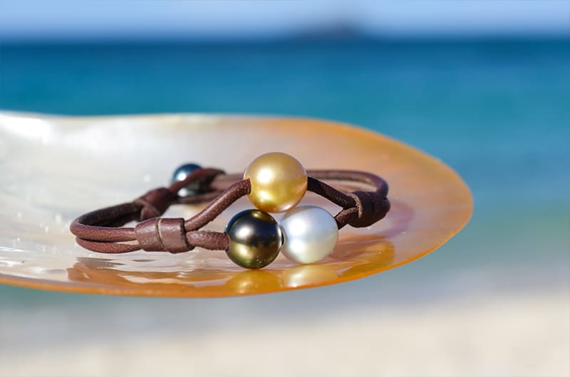 Two-row bracelet with three multicolored pearls displayed on mother-of-pearl facing the sea