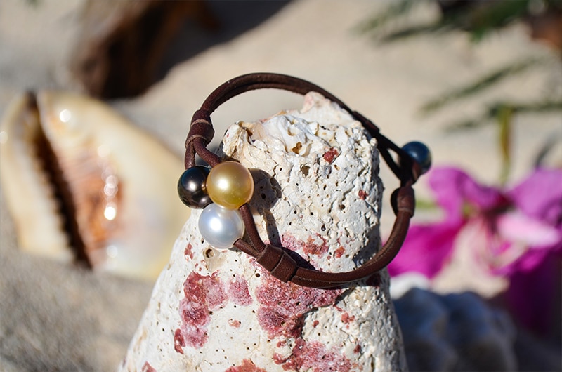 Bracelet with three multicolored pearls displayed around a pale rock near pink flowers