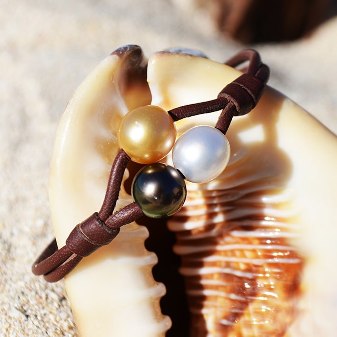 Two-row leather bracelet with three multicolored 9 mm cultured pearls displayed in a seashell