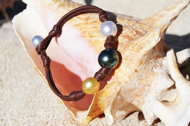 Bracelet with three multicolored pearls and knots displayed in a seashell