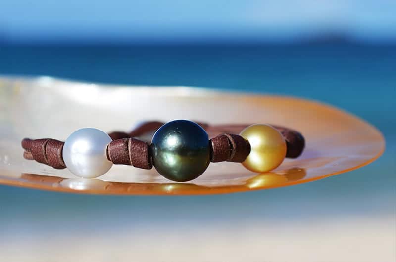 Leather bracelet with three multicolored pearls and knots displayed on mother-of-pearl facing the sea