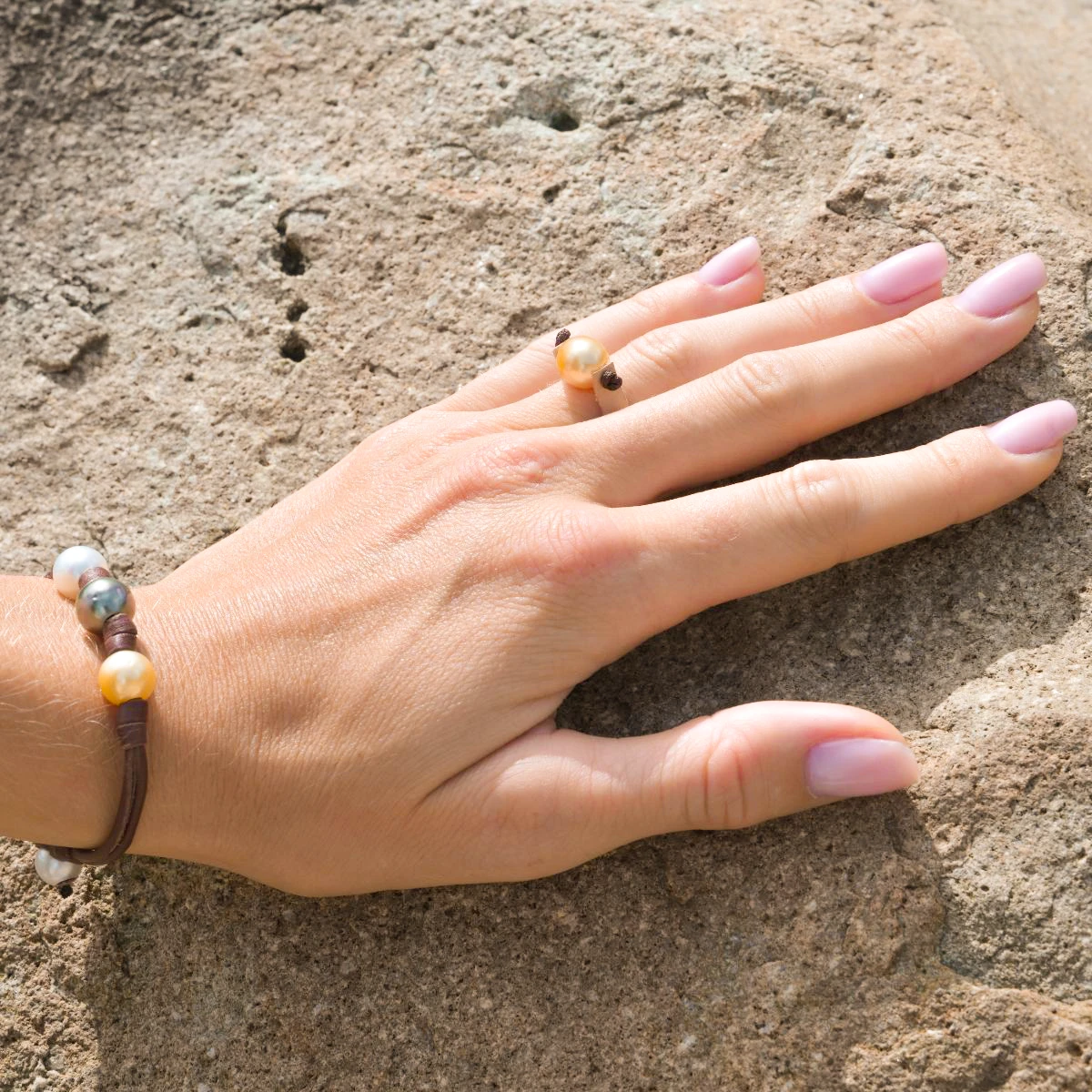 Bracelet with three multicolored pearls worn on the wrist, with the hand resting on a rock