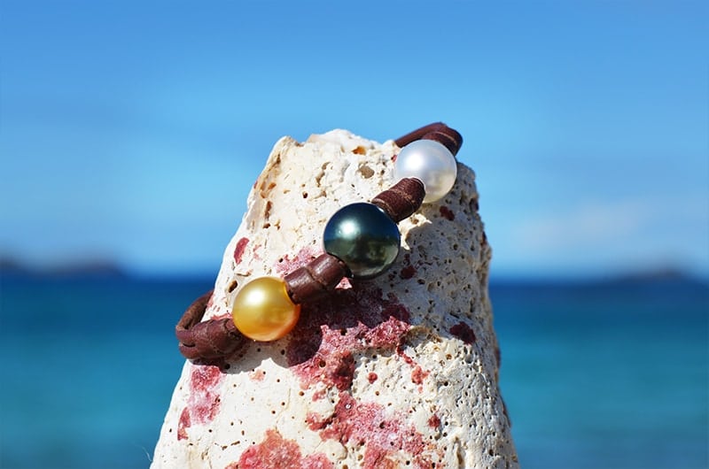 Leather bracelet with three multicolored pearls and knots displayed on a pale rock facing the sea
