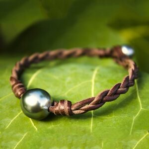 Bracelet en cuir marron tressé avec deux perles de culture de Tahiti présenté sur une feuille verte
