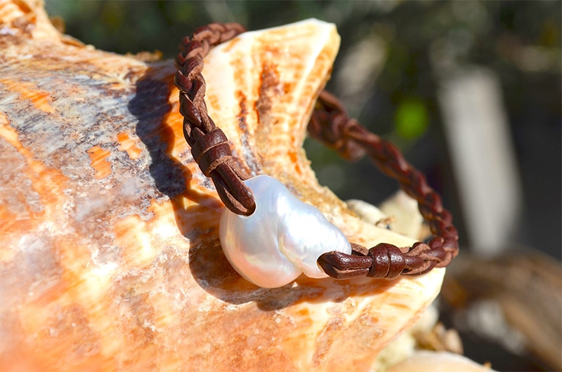 Bracelet en cuir tressé avec une perle d’eau douce blanche présenté sur un coquillage