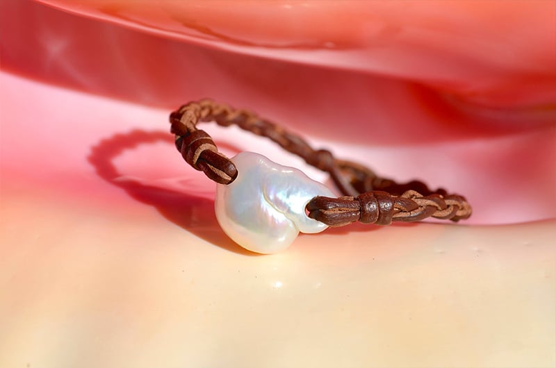 Bracelet en cuir tressé avec une perle d’eau douce blanche présenté sur un fond rose