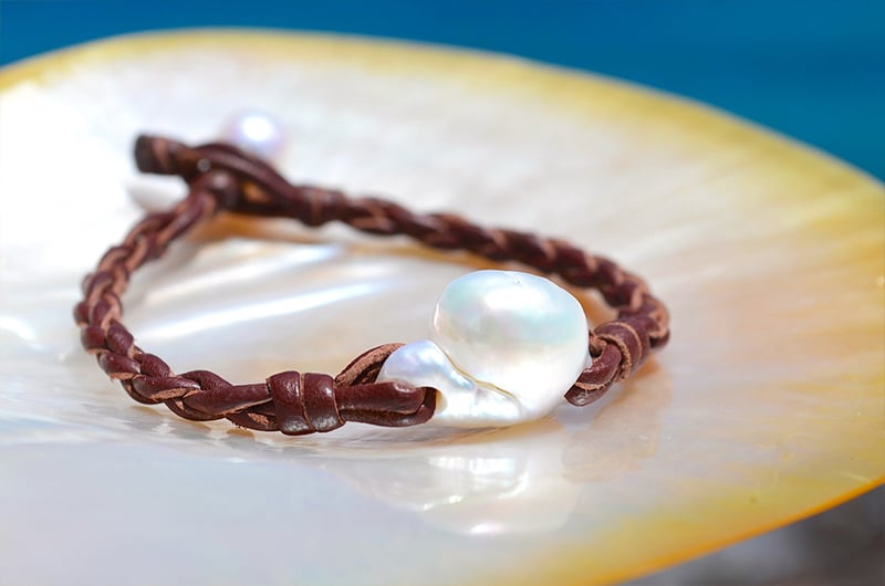 Bracelet tressé avec une perle d’eau douce blanche présenté sur une nacre