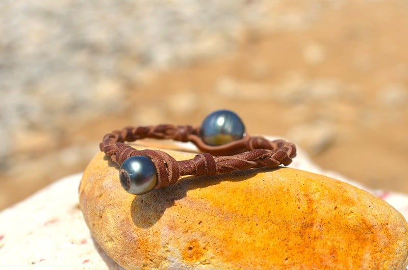 Détail de la perle baroque de Tahiti sur le bracelet en cuir tressé présenté sur un galet