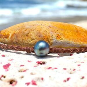 Bracelet tressé avec une perle baroque de Tahiti présenté autour d’un galet face à la mer