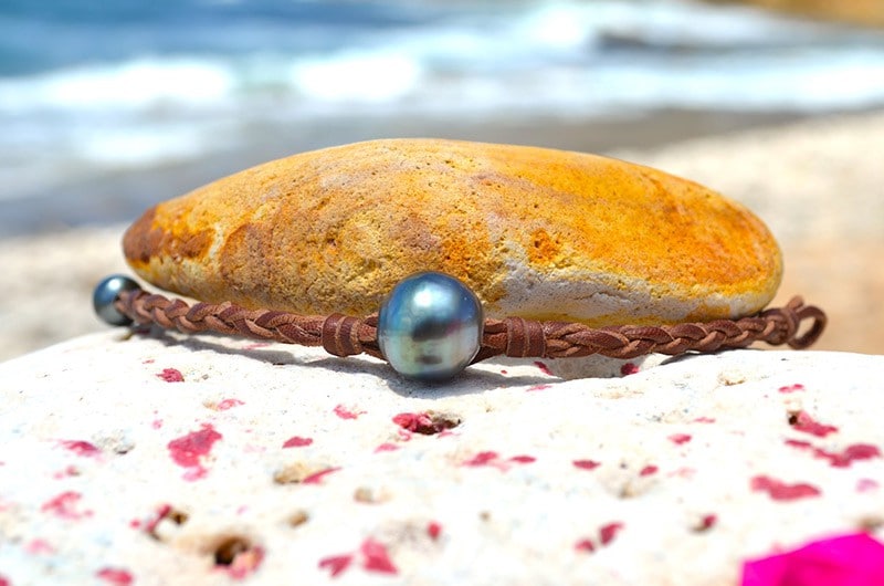 Bracelet tressé avec une perle baroque de Tahiti présenté autour d’un galet face à la mer