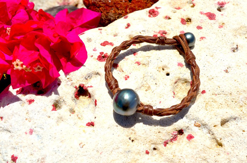 Vue d’ensemble du bracelet tressé avec une perle baroque de Tahiti présenté sur une roche près de fleurs roses