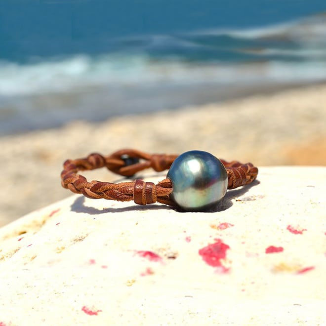 Bracelet en cuir marron tressé avec une perle de culture baroque de Tahiti présenté face à la plage