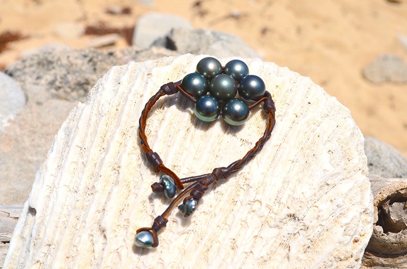 Bracelet tressé avec sept perles de Tahiti présenté sur un grand coquillage à la plage