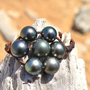 Détail des sept perles de Tahiti du bracelet en cuir tressé présenté sur du bois