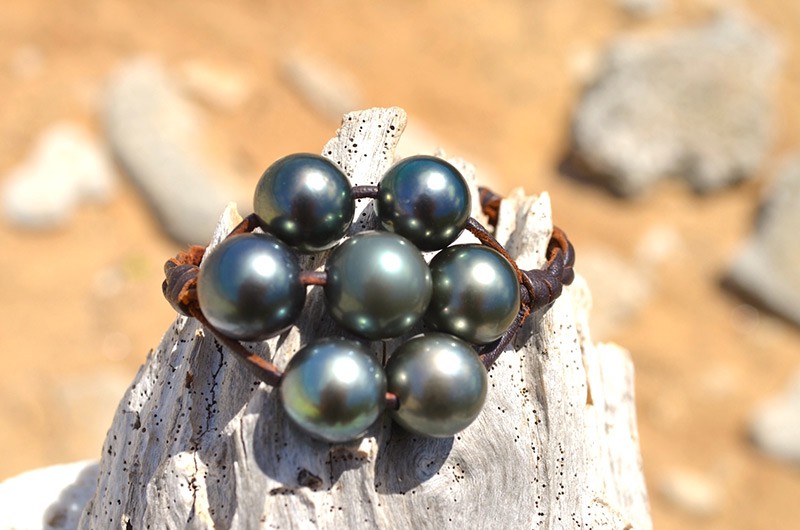 Détail des sept perles de Tahiti du bracelet en cuir tressé présenté sur du bois
