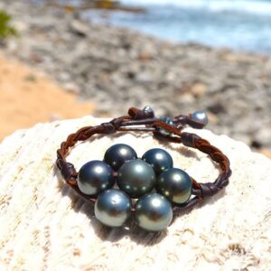 Vue d’ensemble du bracelet tressé avec sept perles de Tahiti présenté sur une roche face à la mer