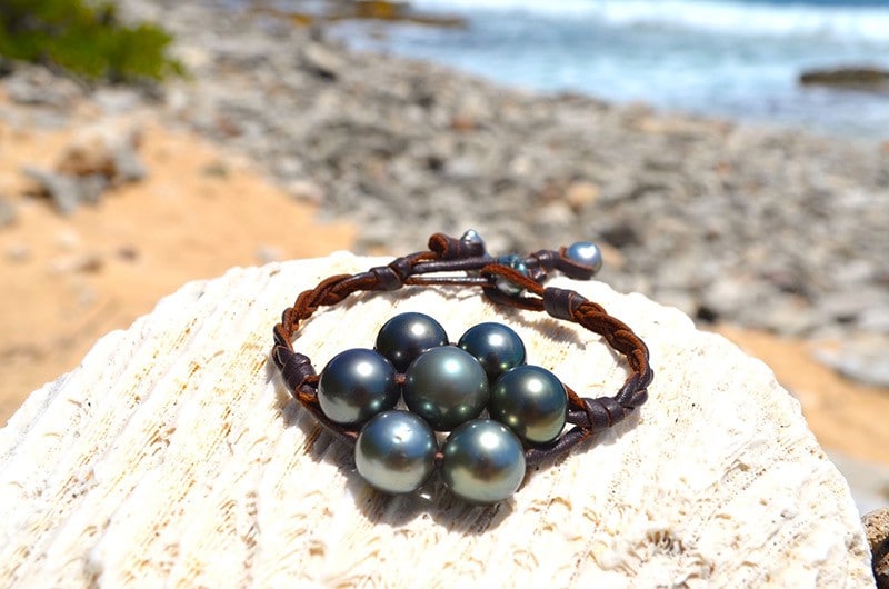 Vue d’ensemble du bracelet tressé avec sept perles de Tahiti présenté sur une roche face à la mer