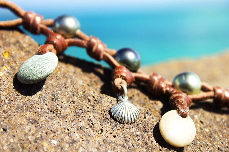 Détail des perles de Tahiti, galets de rivière et breloques du bracelet en cuir présenté sur une roche