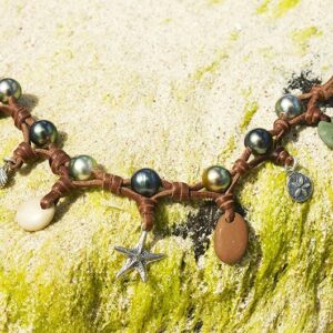 Vue d’ensemble du bracelet avec perles de Tahiti, galets de rivière et breloques présenté sur un filet décoratif