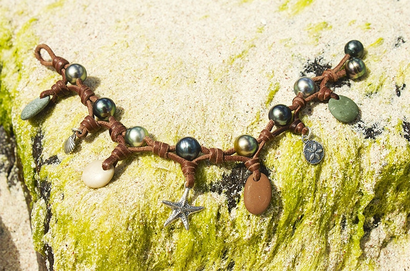 Vue d’ensemble du bracelet avec perles de Tahiti, galets de rivière et breloques présenté sur un filet décoratif