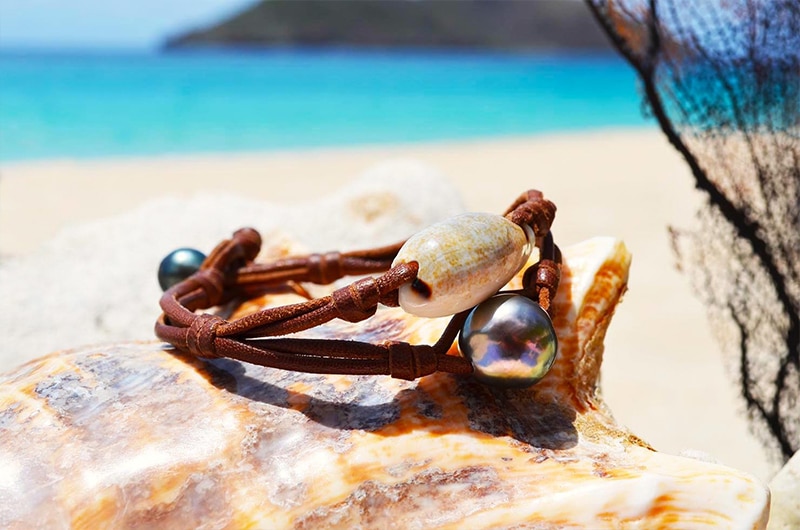 Bracelet avec une perle de Tahiti et un coquillage présenté sur un coquillage près d’un filet décoratif
