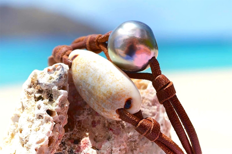 Détail de la perle de Tahiti et du coquillage du bracelet en cuir présenté sur une roche
