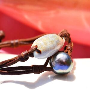 Bracelet en cuir marron avec une perle de culture de Tahiti et un coquillage présenté sur un fond rose