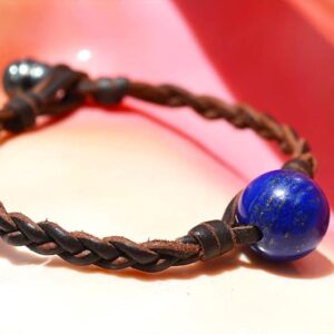 Bracelet en cuir tressé avec lapis-lazuli et perle de Tahiti présenté sur un fond rose