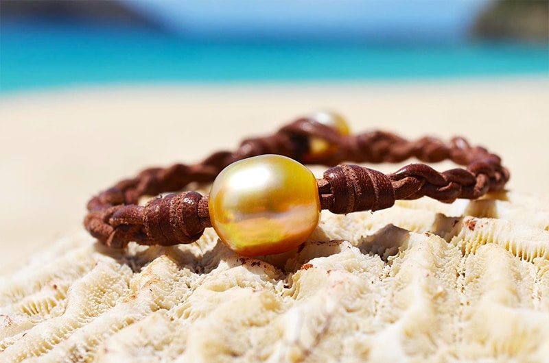 Détail de la perle de culture d’Australie sur le bracelet en cuir tressé présenté sur du corail