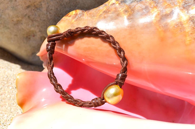 Bracelet tressé avec une perle d’Australie présenté sur un fond rose