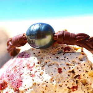 Détail de la perle de Tahiti cerclée sur le bracelet tressé présenté sur une roche