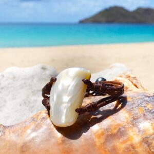 Bracelet en cuir marron avec un grand élément de nacre et des perles de culture de Tahiti présenté sur un coquillage