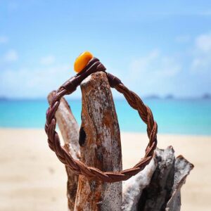 Bracelet en cuir marron tressé avec une perle d’ambre présenté sur du bois face à la mer
