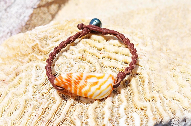 Full view of the bracelet with an orange shell and Tahitian pearl displayed on coral